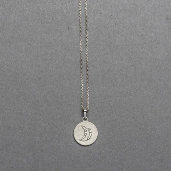 Sterling silver matte-finish coin pendant featuring an embossed crescent moon inset with tiny round diamonds, suspended from a delicate silver cable chain