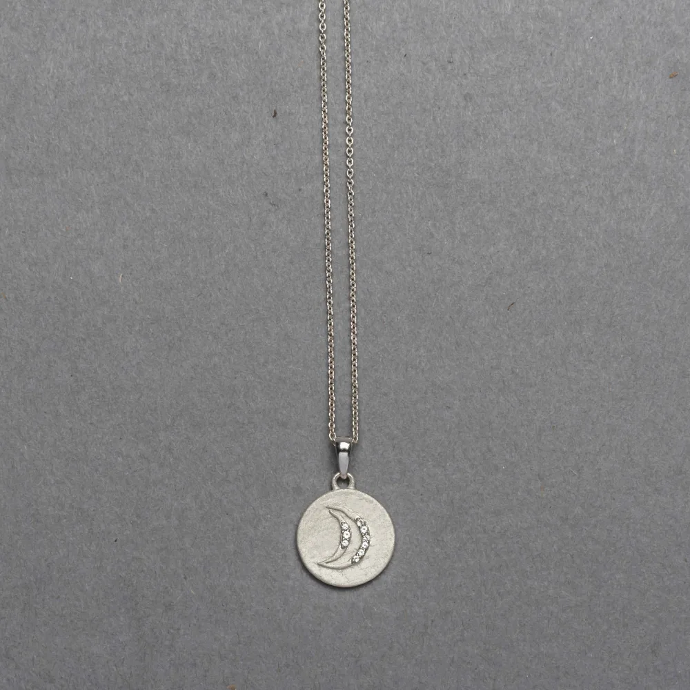 Sterling silver matte-finish coin pendant featuring an embossed crescent moon inset with tiny round diamonds, suspended from a delicate silver cable chain