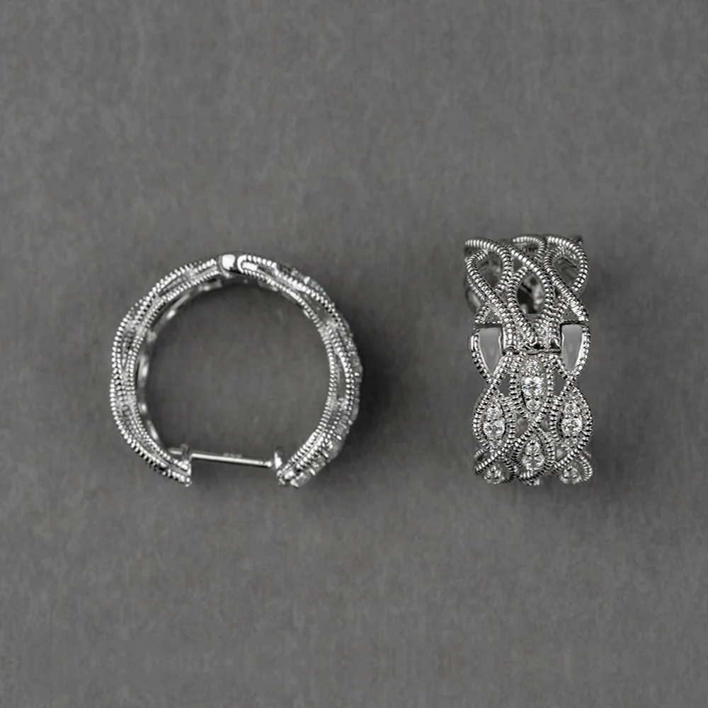Pair of wide white gold or silver huggie hoop earrings featuring an intricate vintage-style openwork lattice design with milgrain beading and pavé-set clear stones.