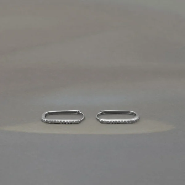 A pair of wide silver-toned huggie hoop earrings featuring an intricate, vintage-style openwork lattice design with milgrain beading and pavé-set clear gemstones.