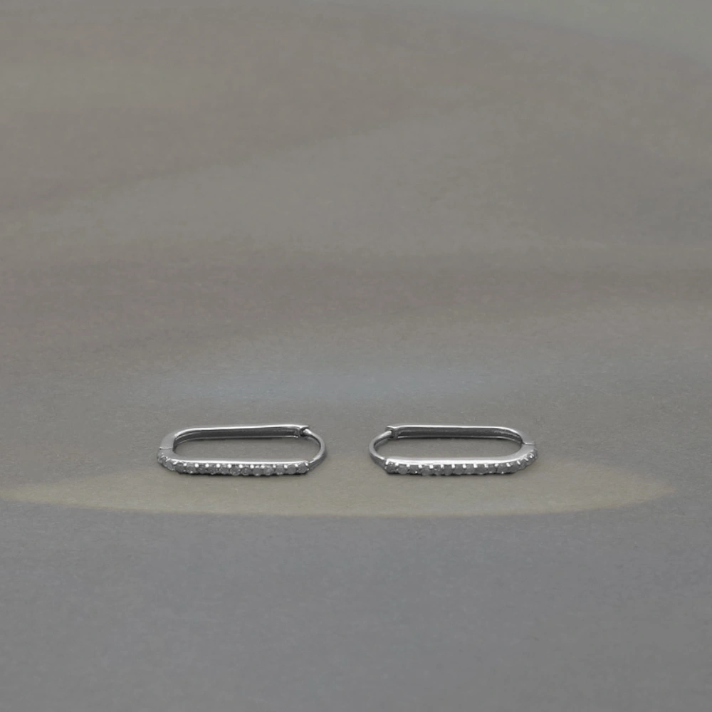 A pair of wide silver-toned huggie hoop earrings featuring an intricate, vintage-style openwork lattice design with milgrain beading and pavé-set clear gemstones.