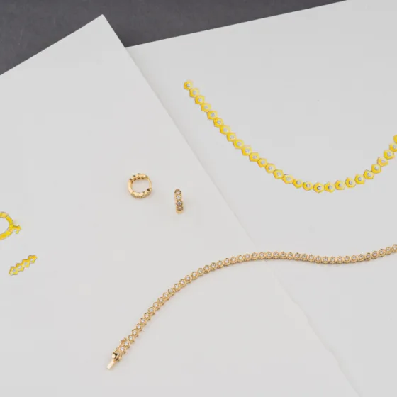Gold-plated jewelry set with a honeycomb design necklace, tennis bracelet, and huggie earrings on white papers.