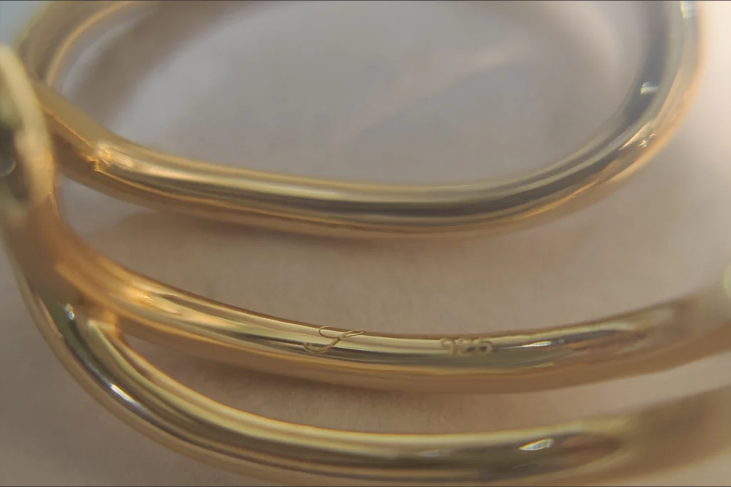 Extreme macro shot of a gold-plated ring's inner band showing custom cursive initials and a 925 hallmark stamp.