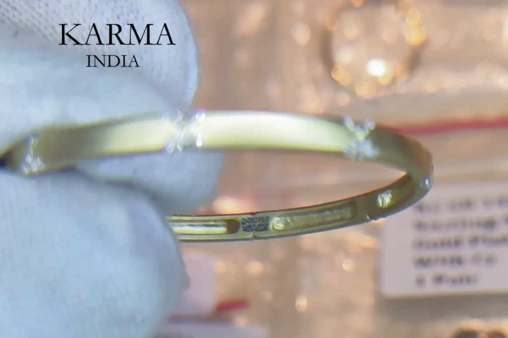 Gloved hand holding a gold-plated bangle bracelet with small diamond accents, showcasing internal hallmark stamps.